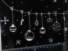 black and white photograph of christmas ornaments hanging on a line with snowflakes in the background