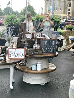 two women standing in front of a table with some items on it and one holding a sign that says come in awesome