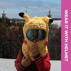 a young boy wearing a knitted animal hat and goggles while holding his nose to his mouth