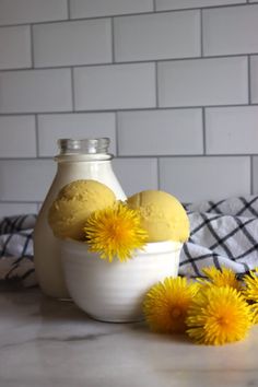 some yellow flowers are in a white bowl on a counter next to a bottle and towel