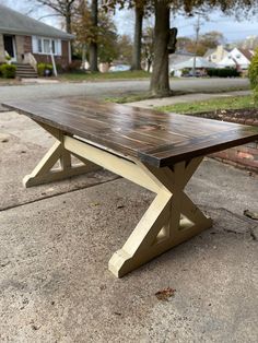 a wooden table sitting in the middle of a sidewalk next to a tree and house