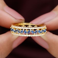 a woman's hand holding a gold ring with blue and white stones