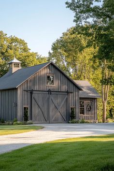 a barn with two doors and windows in the middle of a grassy area next to trees