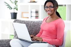 a woman sitting on a couch with a laptop computer in her lap and smiling at the camera