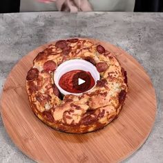 a pizza sitting on top of a wooden plate next to a bowl of ketchup