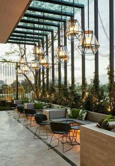 an outdoor dining area with tables and chairs, plants on the wall and lights hanging from the ceiling