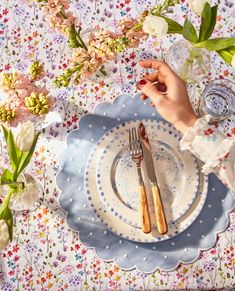 a person holding a knife and fork over a plate on a floral tablecloth with flowers