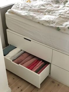 an open drawer with folded towels in it next to a white bed and wooden floor