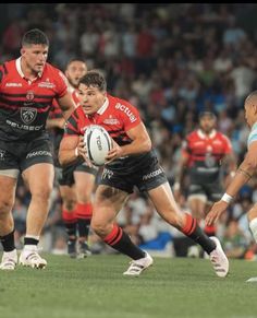 two rugby players are running with the ball in their hands as others watch from the sidelines