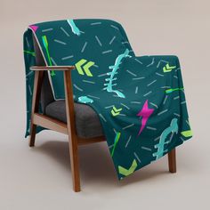 a chair with a blanket on it that has arrows and birds all over it, sitting in front of a gray background