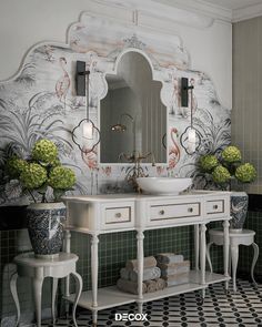 a white sink sitting under a mirror next to two vases filled with green flowers