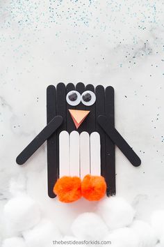 a penguin made out of popsicle sticks on top of some cotton balls and yarn