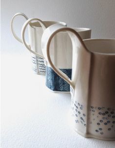 three ceramic pitchers are lined up on a white counter top, one is blue and the other is beige