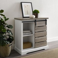 a white and grey cabinet with drawers next to a potted plant on the floor