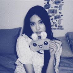 a woman holding a stuffed animal in her hand and posing for the camera while sitting on a bed