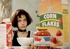 a woman sitting at a table in front of a jar of cornflakes and a bowl of fruit