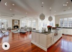 a large open kitchen and living room with hardwood floors, white walls, and windows