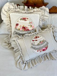 two decorative pillows on a bed with ruffles and flowers in the pillow cases