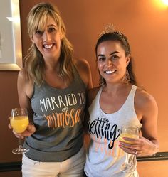 two beautiful women standing next to each other holding glasses of wine and orange juice in their hands