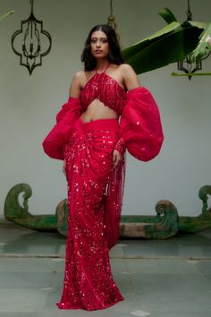 Step into iconic glamour where elegance is draped in the shimmer of scarlet palette for the season’s soirees. Our new-age concept of pre-draped saree features a chic halter neck blouse adorned with nalki crystals embellishment paired up with a sequined pre-draped skirt. Adding a hint of drama the handmade puffer sleeves complete the whole iconic look. • Pre-draped sequined skirt.• Halter-neck blouse adorned with nalki crystals and moti embellishments. • Metal hook at the back side of the blouse to conceal. • Puffed sleeves with an attached sequined dupatta.• Metal zip on the backside of the skirt along with a hook for support.From Moledro’s Fitoor collection. DELIVERY TIMEPlease allow 8-12 weeks for your outfit to arrive. FABRIC DETAILSBlouse: Butterfly Net Skirt: GeorgetteSleeves: Net Pro Modern Indian Wedding Guest Outfit, Ladies Sangeet Outfit, Butterfly Skirt Outfit, Roka Outfits, Skirt Saree, Halter Neck Blouse, Ladies Sangeet, Modern Indian Wedding, Halter Neck Blouses