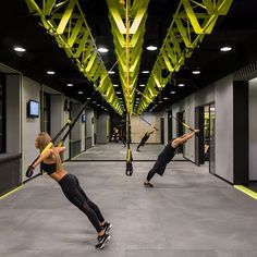 two women are doing exercises in an indoor gym with yellow beams overhead, while one woman is holding a baseball bat