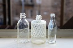 three empty glass bottles sitting on top of a window sill next to each other