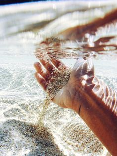 someone is holding their hand out in the water with sand all over them and texting