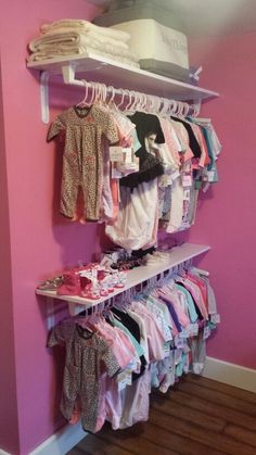 a baby's clothing rack in the corner of a room with pink walls and wooden floors