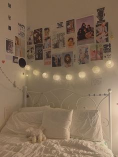 a white bed with lots of pictures on the wall above it and lights hanging from the headboard