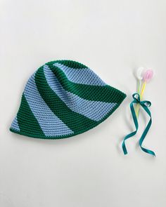 a crocheted hat next to a flower on a white surface with green and blue stripes