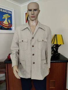 I'm listing some safari and leisure suits and jackets. This one is from the 70s by Fletcher Jones in a beige wool polyester and linen combination. It has long sleeves with cuffs, a four button closure with caramel buttons, two chest pockets with flaps and buttons and two hip pockets echoed with buttons. The condition is very good Measurements are  shoulder to shoulder 45cm Chest 112cm Sleeves shoulder to cuff 63cm Length shoulder to hem 73cm Casual Beige Sport Coat With Flap Pockets, Vintage Beige Utility Jacket With Button Closure, Classic Beige Utility Jacket With Flap Pockets, Vintage Beige Utility Jacket With Pockets, Beige Utility Jacket With Flap Pockets And Lapel Collar, Beige Collared Utility Jacket With Flap Pockets, Beige Long-sleeved Sport Coat With Flap Pockets, Vintage Khaki Blazer With Pockets, Beige Collared Utility Jacket With Pockets