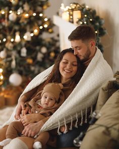 a man and woman sitting on a couch with a baby wrapped in a blanket