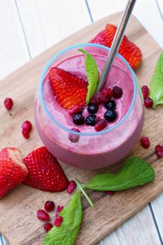 a smoothie with strawberries and blueberries is on a cutting board next to some leaves