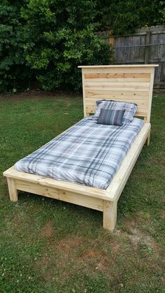 a bed frame made out of wood with plaid sheets and pillows on it in the grass