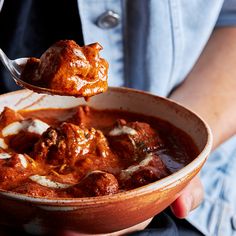 a person is holding a spoon full of meatballs and tomato sauce in a bowl