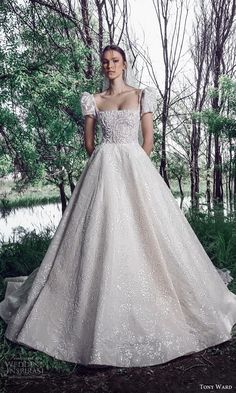 a woman wearing a wedding dress in the woods with trees and grass behind her is looking at the camera