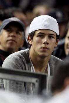 a young man wearing a white hat sitting next to other people at a tennis match