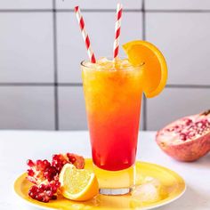 a drink with orange slices and straws on a yellow plate next to pomegranate