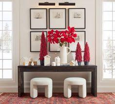 a table topped with red poinsettias and two white stools next to a wall