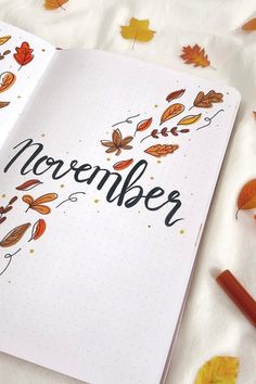 an open notebook with the word november written on it next to autumn leaves and pencils