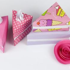 three different types of folded paper on a white surface with a pink flower next to it