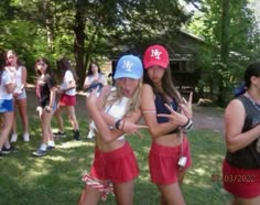 two girls in red shorts and blue caps are standing on the grass with their hands up