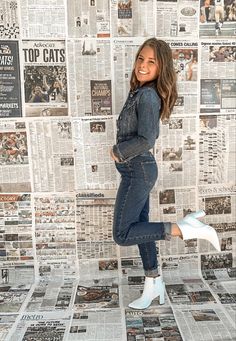 a woman standing in front of a wall covered with newspapers