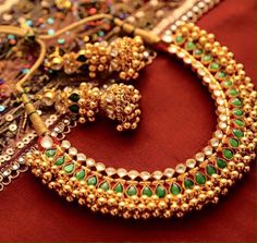 an assortment of jewelry is displayed on a red tablecloth with gold and green accents