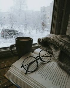 a cup of coffee and some books on a window sill near a snowy field