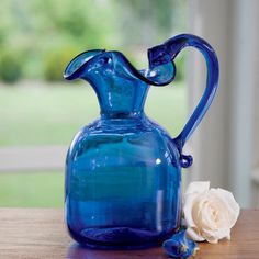 a blue glass pitcher sitting on top of a wooden table next to a white rose