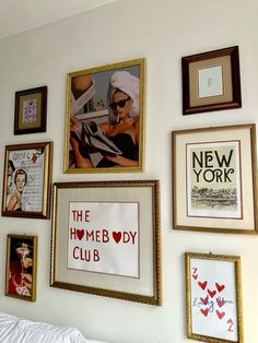 many framed pictures hang on the wall above a bed