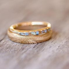 two gold wedding bands with opal stones on top of each other sitting on a wooden surface