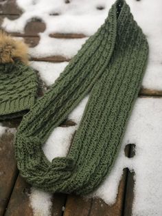 a knitted scarf and hat sitting on top of snow covered wooden planks in the snow