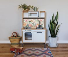 a toy kitchen set with a potted plant next to it and a rug on the floor